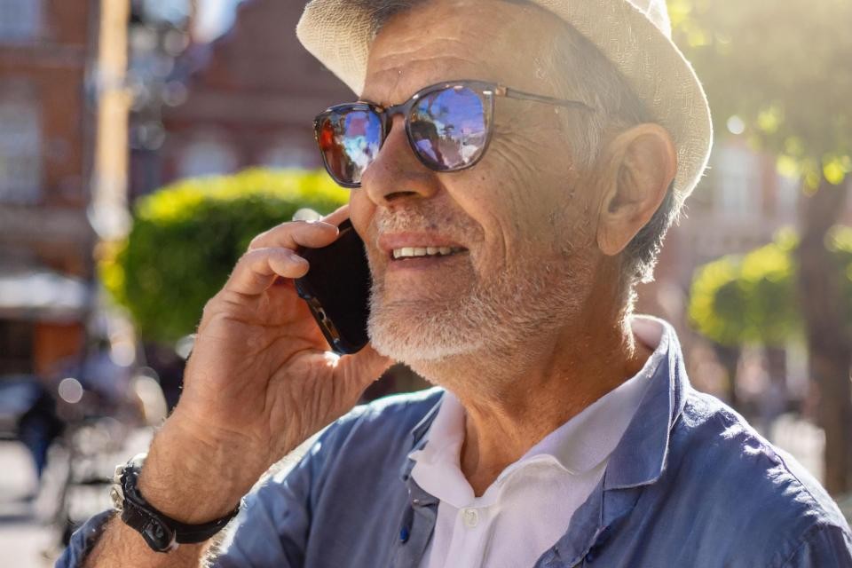 Ein älterer Mann mit Sonnenhut hält sein Handy am Ohr.