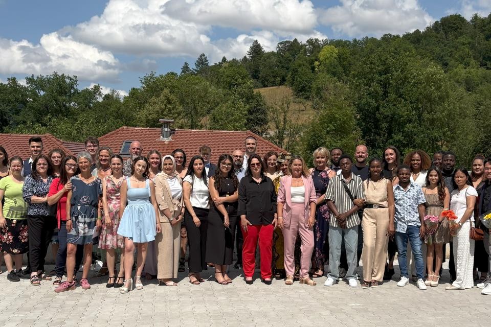 Im Vordergrund stehen Schülerinnen und Schüler in Abendgarderobe, rechts und links davon Lehrer und Schulleiter. Im Hintergrund sind grüne Bäume.