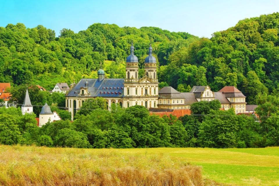 Der Klosterkomplex in Kloster Schöntal mit der Klosterkirche mit den beiden imposanten Türmen. Um das Kloster befindet sich viel Wald und Felder.