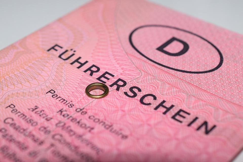 Ein älterer Deutscher Führerschien ist zu sehen. Ein rosa gefaltetes Papierheft. Oben steht der Buchstabe "D" in einem ovalen Kreis. Darunter "Führerschein" in Großbuchstaben. Darunter ist ein Loch mit Ring. Die weitere Schrift darunter ist unscharf.
