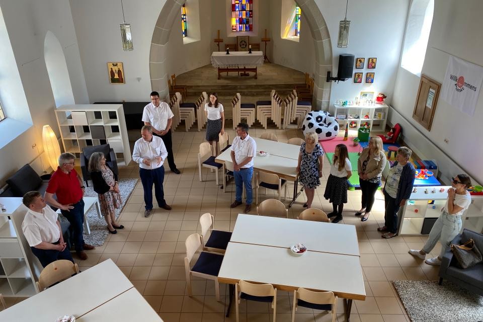In einer Kirche stehen Tischgruppen und Stühle; Teppiche liegen auf dem Boden und eine Spielecke ist eingerichtet. 