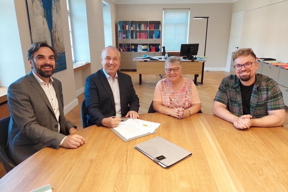 Vier Personen sitzen an einem Tisch und unterzeichnen den Vertrag