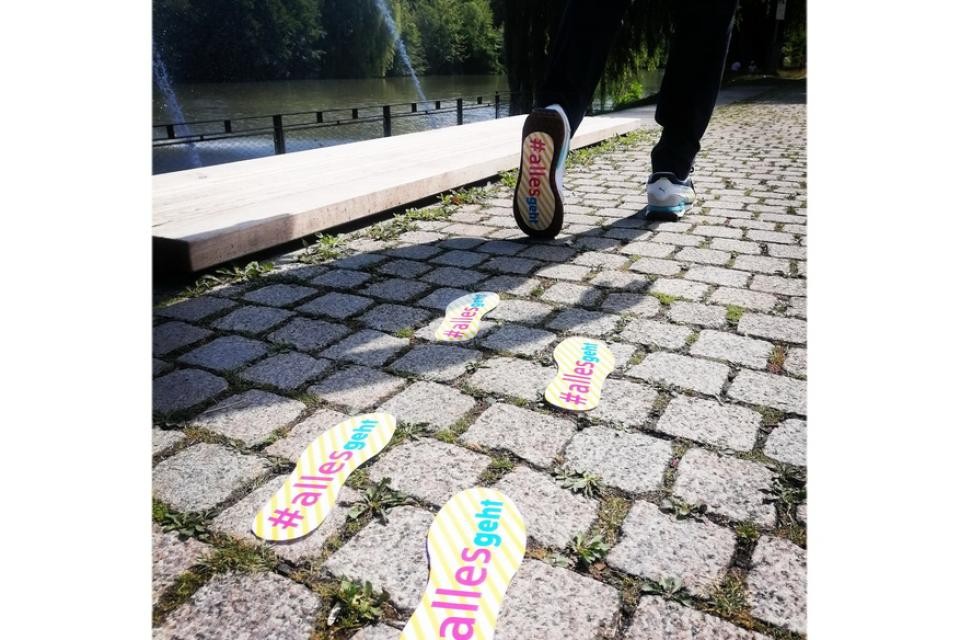 Symbolbild: Ein Fußgänger hinterlässt bunte Fußspuren auf dem Weg.