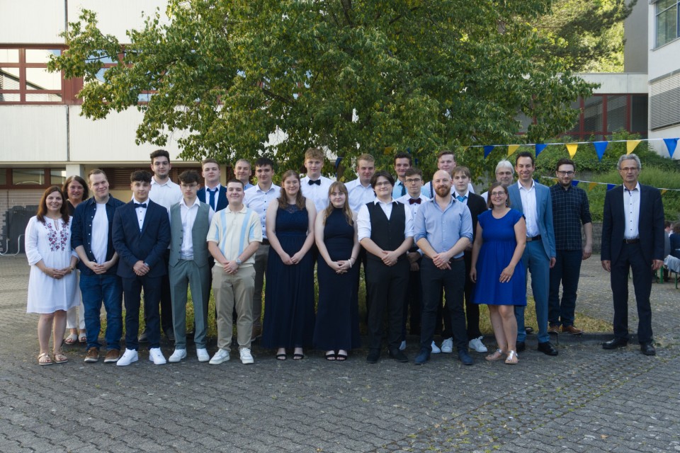 Gruppenfoto der Abiturienten. Im Hintergrund ist das Schulgebäude sowie ein Baum zu sehen.