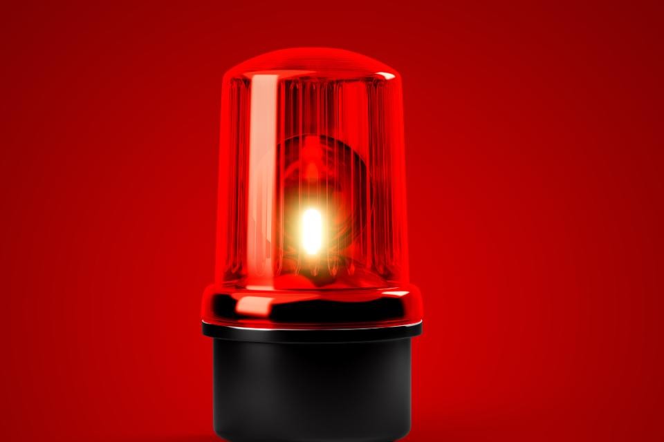 Im Hintergrund blauer Himmel, im Vordergrund links ein grauer Lautsprecher, rechts davon eine Sirene in rot-grau. Beides ist auf einem Mast verbaut.