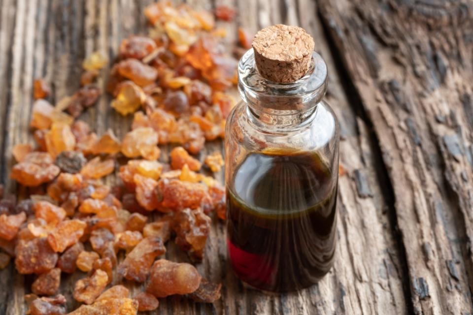 Durchsichtiges Gläschen mit brauner Flüssigkeit darin. Brauner Korkverschluss. Links daneben brauner Rohrohrzucker. Darunter braunes Holz mit Maserung.