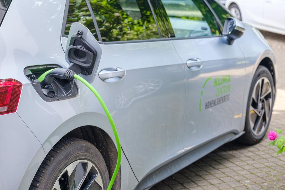 Ein graues E-Auto wird mit Strom über ein grünes Kabel geladen.