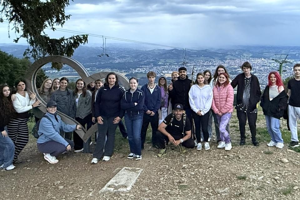 Eine Gruppe von Personen an einem Aussichtspunkt. Links befindet sich ein großes Herz aus Holz. Im Hintergrund ist in der Ferne eine Stadt zu sehen.