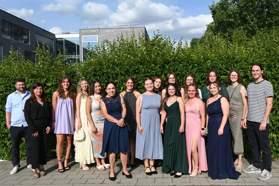 Eine Gruppe von Personen mit bunten Abendkleidern vor einer grünen Hecke.