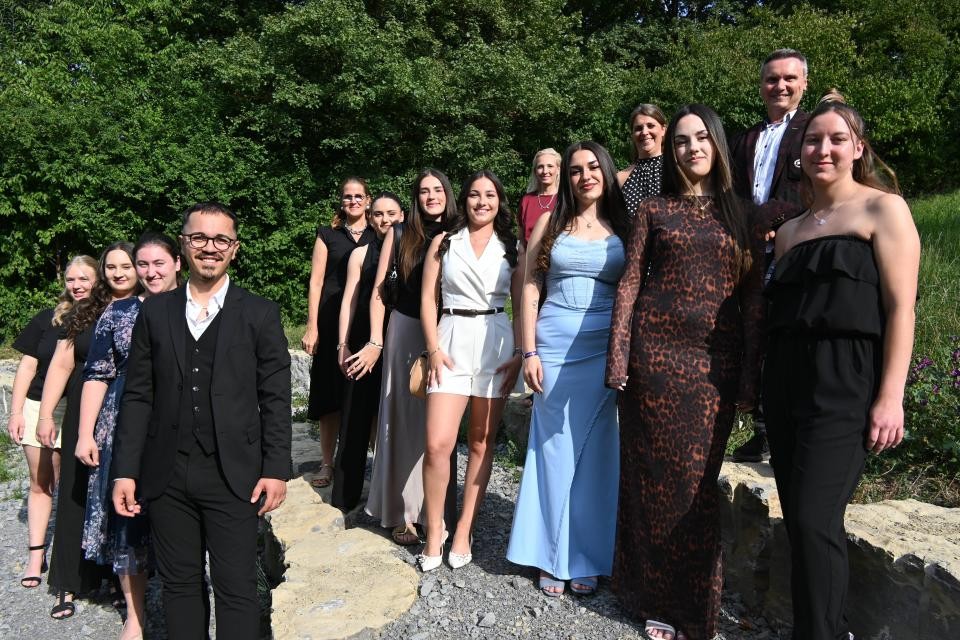 Eine Gruppe von Personen mit bunten Abendkleidern vor einer grünen Hecke.