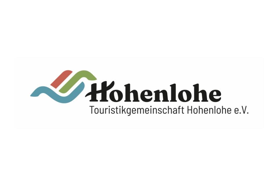 Logo der Touristikgemeinschaft Hohenlohe. Schwarze Schrift Hohenlohe. Darunter der Slogan: Im Süden ganz oben. An der linken Seite drei Linien in rot, grün und blau, die Berge und Täler darstellen.