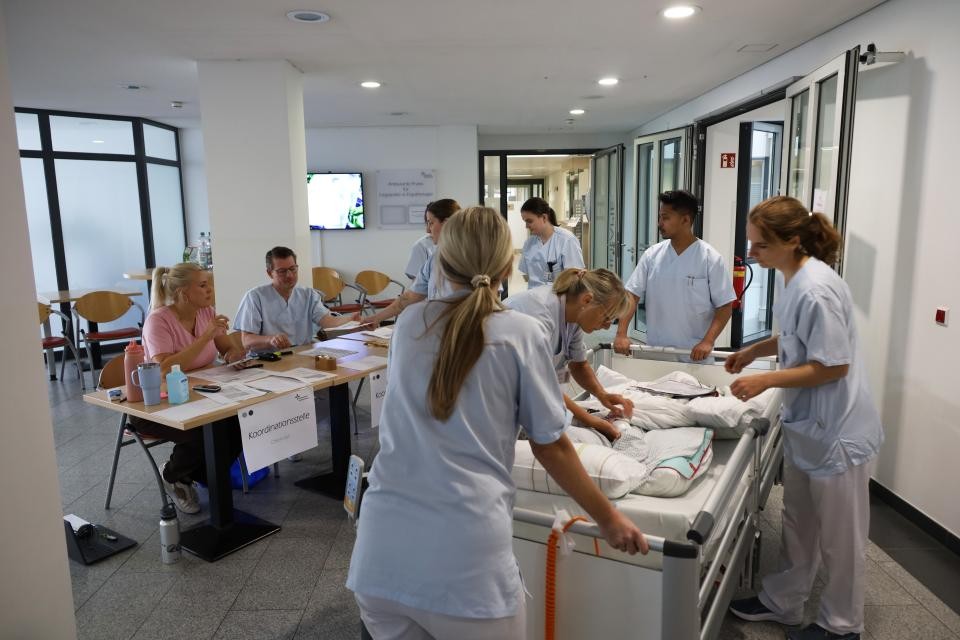 Mehrere Krankenschwestern stehen um ein Krankenbett, eine Schwester entfernt das alte Patientenarmband