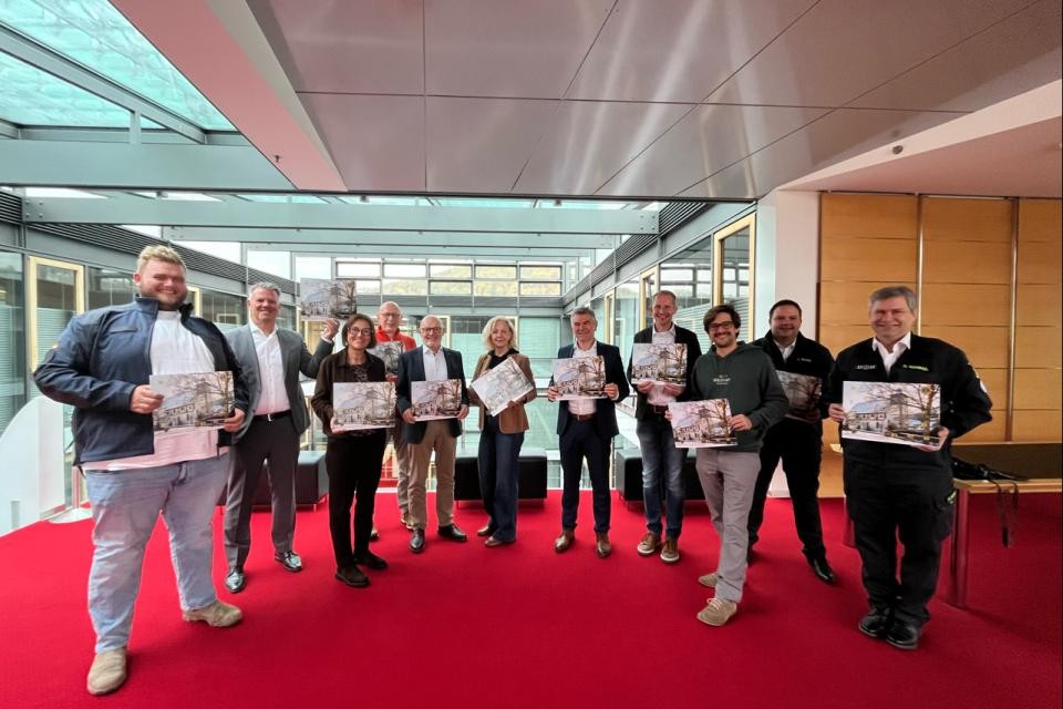 Gruppenbild mehrerer Menschen stehen im einem Raum mit rotem Teppichboden, die Personen halten den Hohenloher Adventskalenders 2026 in der Hand.