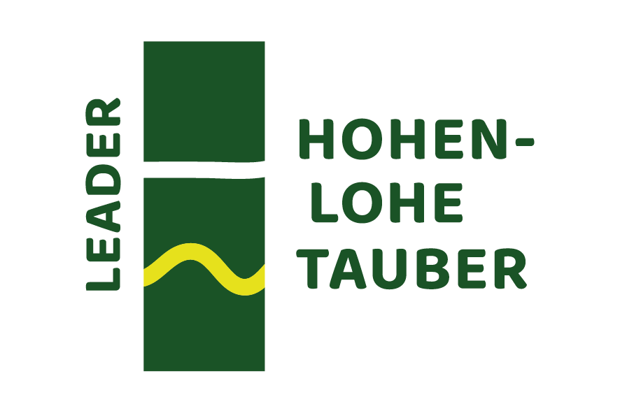 Logo des Förderprogramms Leader Hohenlohe-Tauber. Dunkelgrüne Schrift auf weißem Hintergrund: Leader Hohenlohe-Tauber. Mittig zwei dunkelgrüne Rechtecke. Hellgrüne Welle im unteren Rechteck.