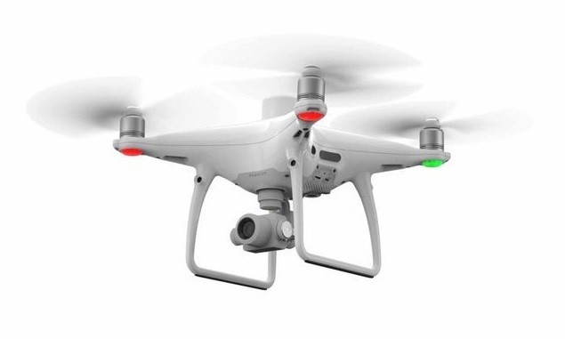 Eine Drohne mit vier Propellern, unterhalb ist eine Kamera angebracht. Unter den Propellern sind rote und grüne Lichter angebracht. Die Drohne ist weiß.