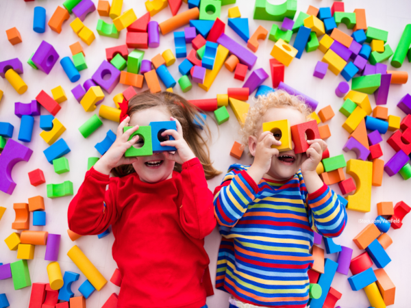 zwei Kinder liegen zwischen bunten Bauklötzen auf dem Boden